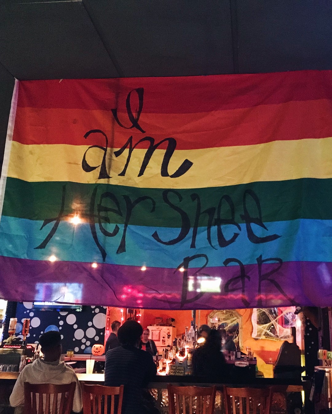 Pride flag at a bar with the text "her shee bar"